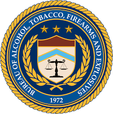 Official seal of the Bureau of Alcohol, Tobacco, Firearms and Explosives featuring a blue background, golden laurel wreath, and scales of justice symbol.